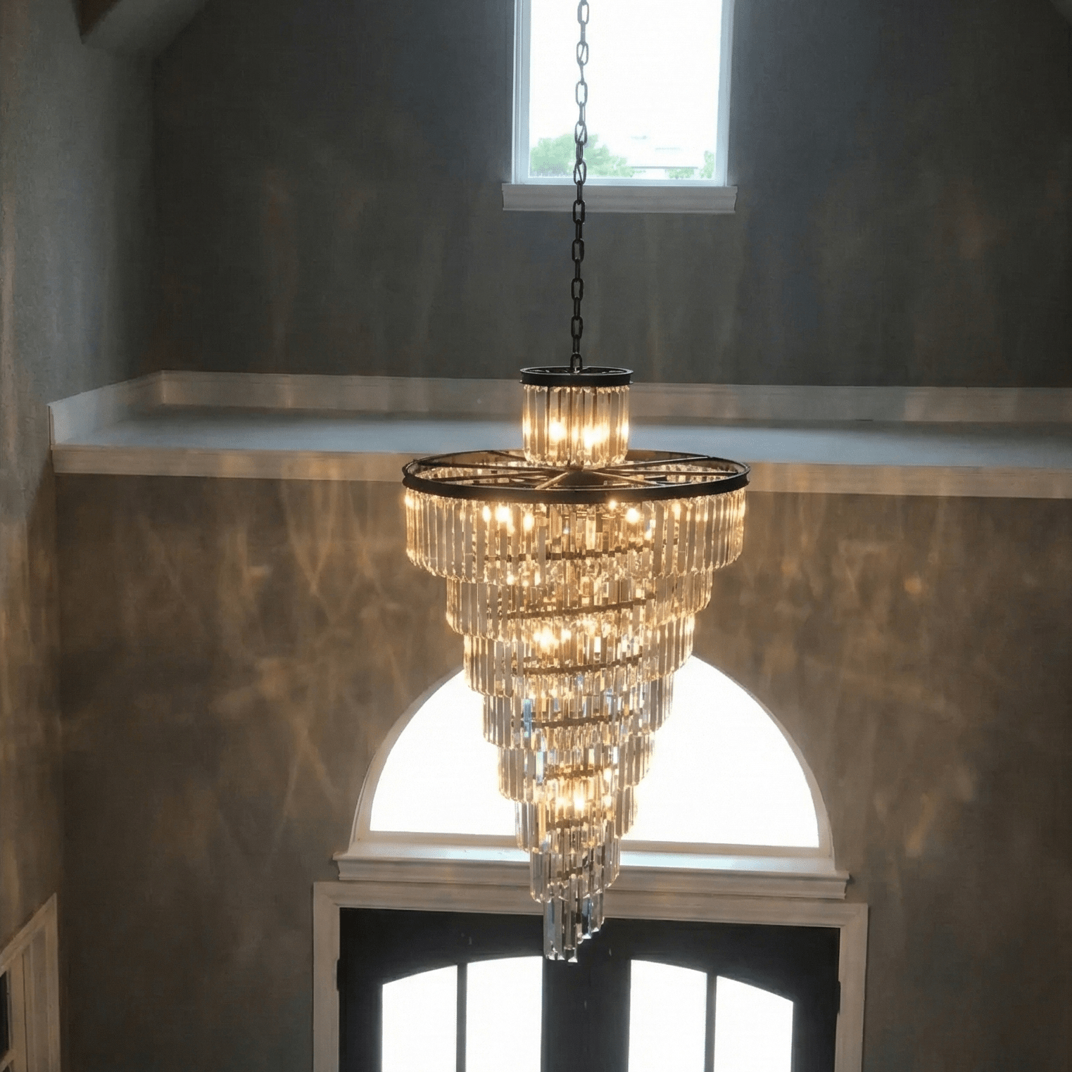 Veccini Odeon spiral tiered crystal chandelier hanging in a grand foyer staircase with high ceiling and arched entryway